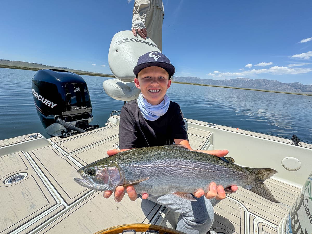 A smiling fly fisherman holding a large brown trout on the Crowley Lake near Mammoth Lakes, CA.