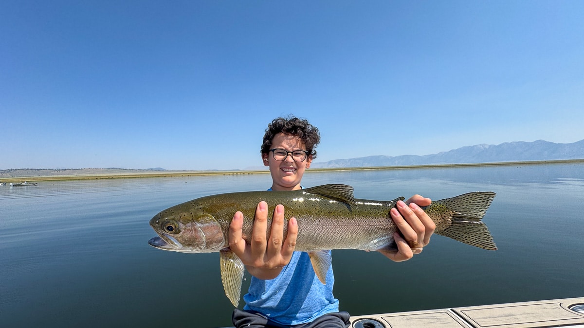 A fly fisherman holding a large brown trout on Crowley Lake near Mammoth Lakes, CA