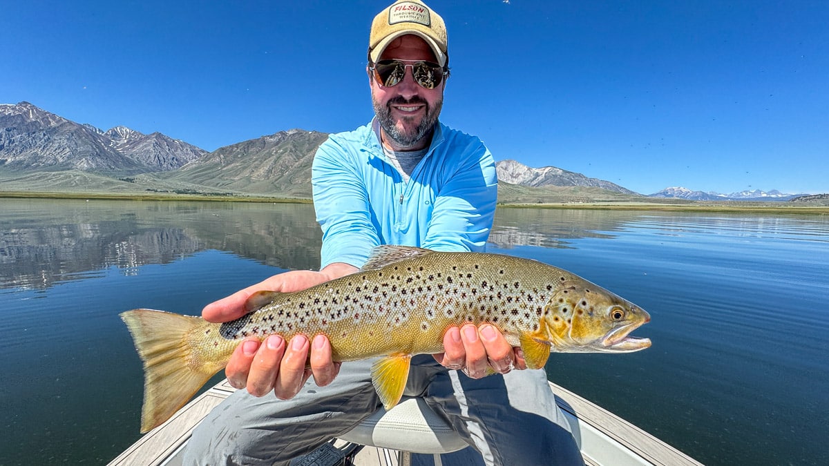 A fly fisherman holding a large rainbow trout on Crowley Lake near Mammoth Lakes, CA