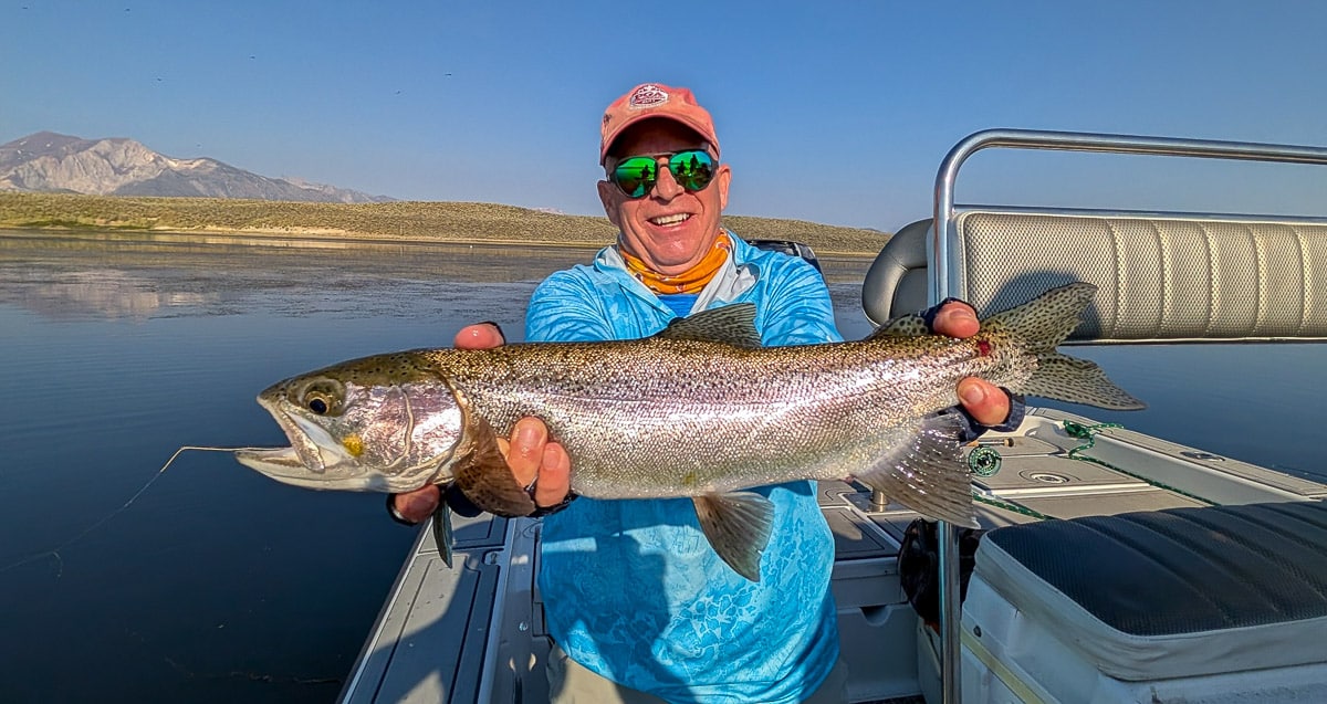 A fly fisherman holding a large rainbow trout on Crowley Lake near Mammoth Lakes, CA