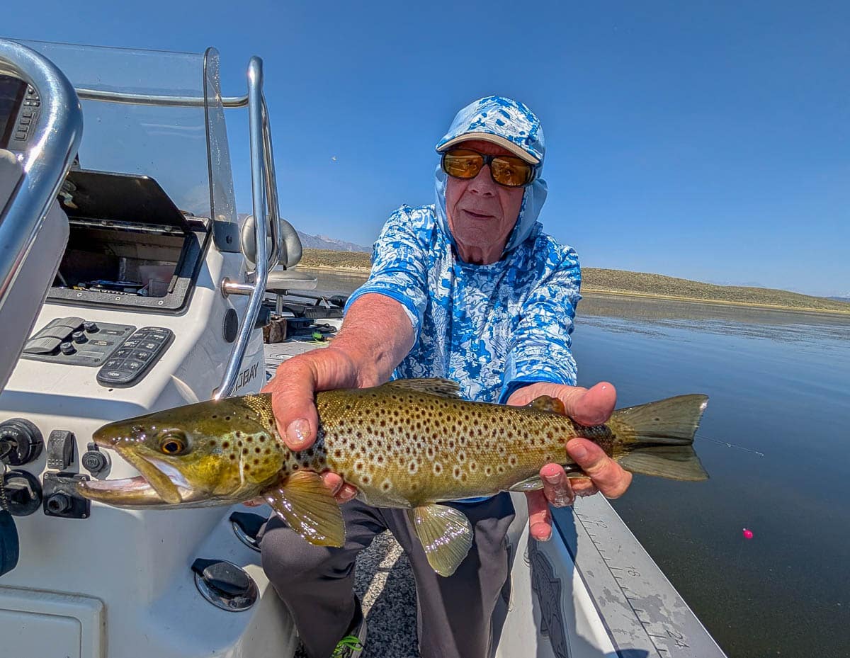 A fly fisherman holding a large rainbow trout on Crowley Lake near Mammoth Lakes, CA