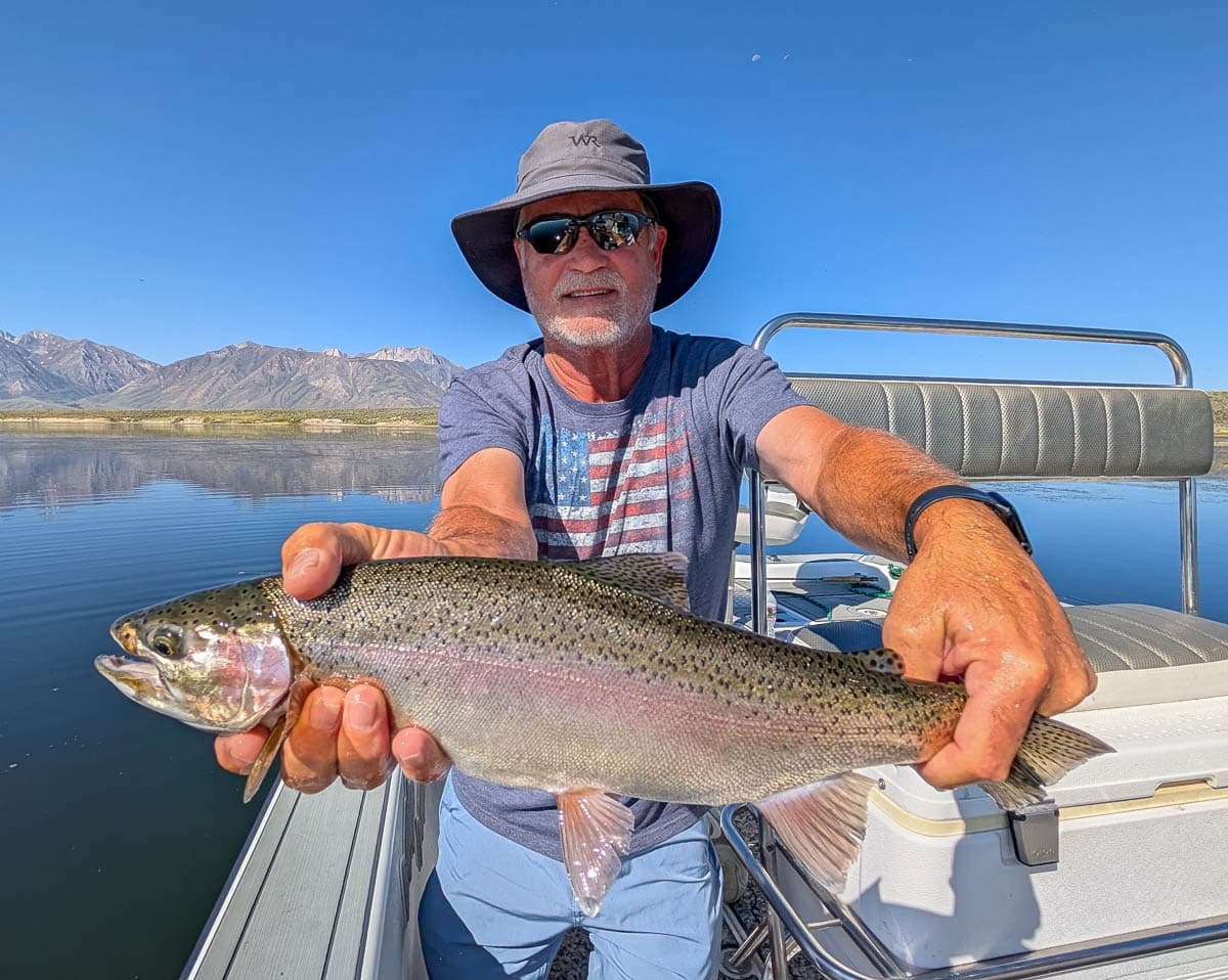 A fly fisherman holding a large rainbow trout on Crowley Lake near Mammoth Lakes, CA