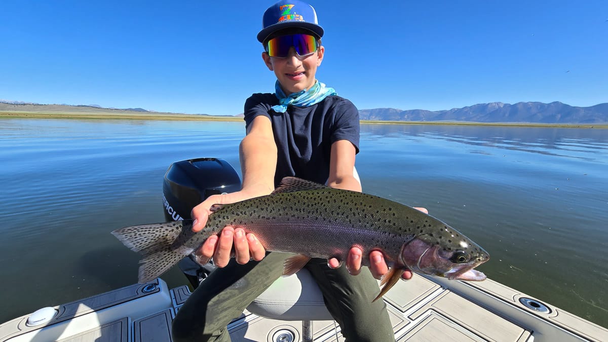 A smiling fly fisherman holding a large rainbow trout on the Crowley Lake near Mammoth Lakes, CA.