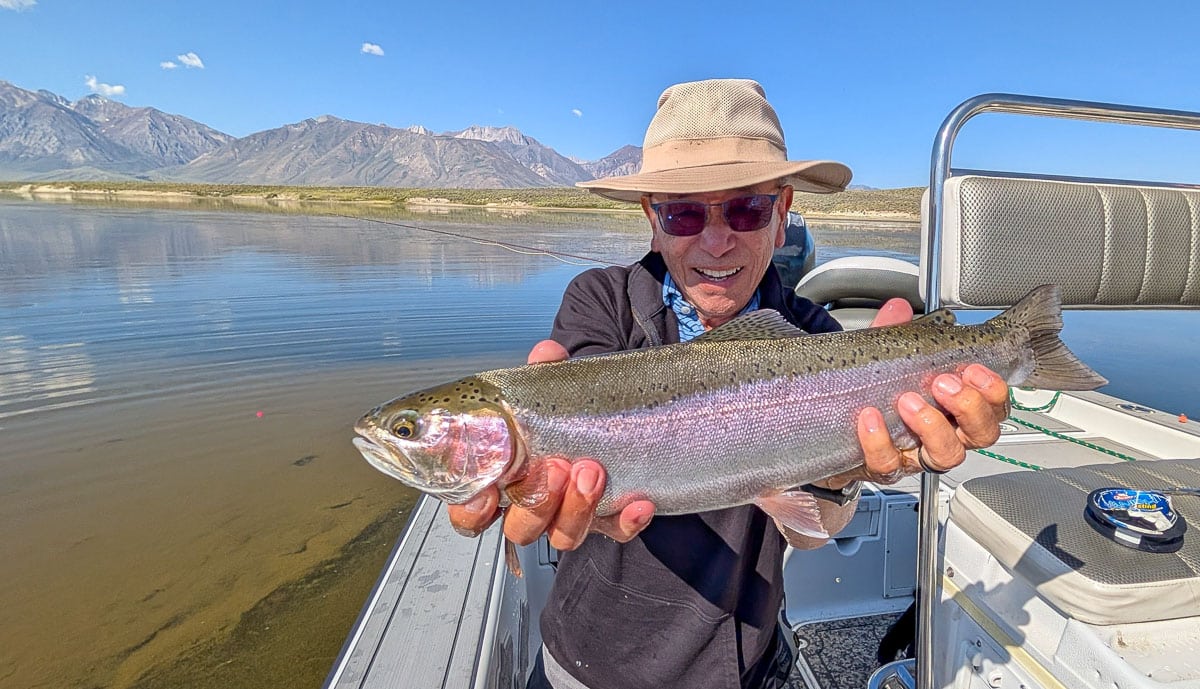 A fly fisherman holding a large rainbow trout on Crowley Lake near Mammoth Lakes, CA.