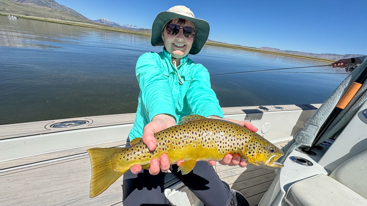 A smiling fly fisherman holding a large rainbow trout on the Crowley Lake near Mammoth Lakes, CA.
