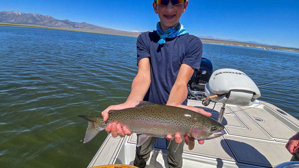 A fly fisherman holding a large rainbow trout on Crowley Lake near Mammoth Lakes, CA