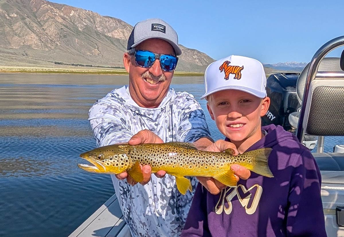 A smiling fly fisherman holding a large rainbow trout on the Crowley Lake near Mammoth Lakes, CA.