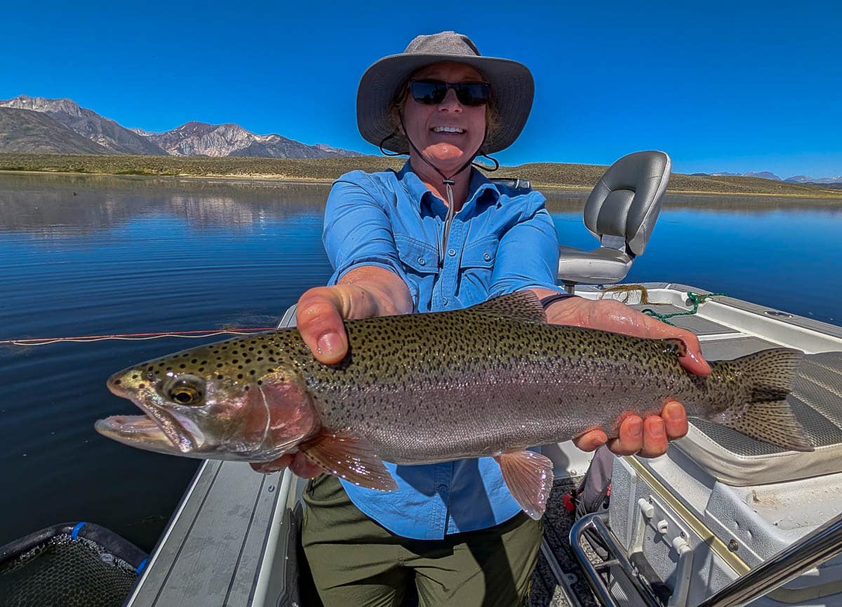 A fly fisherwoman holding a large rainbow trout on Crowley Lake near Mammoth Lakes, CA