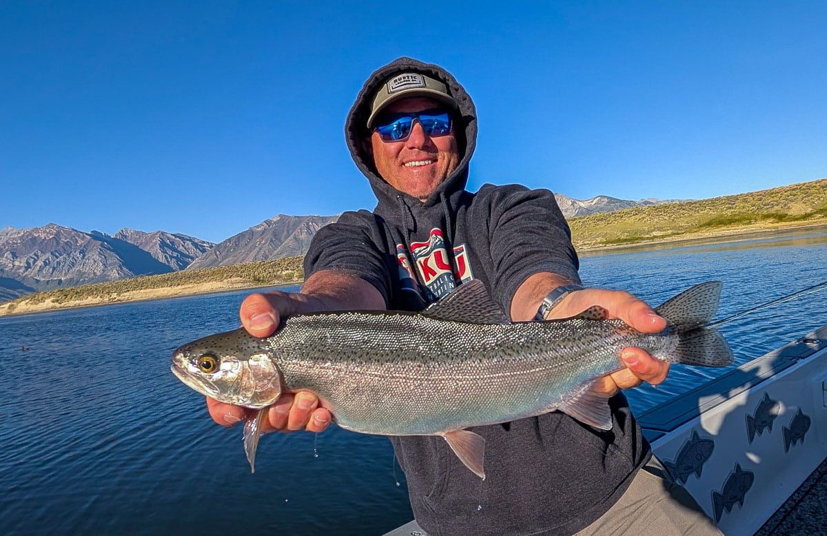 A smiling fly fisherman holding a large brown trout on the Crowley Lake near Mammoth Lakes, CA.