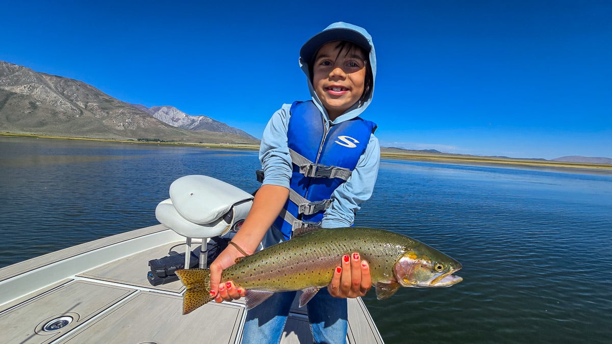 A fly fisherman holding a large rainbow trout on Crowley Lake near Mammoth Lakes, CA