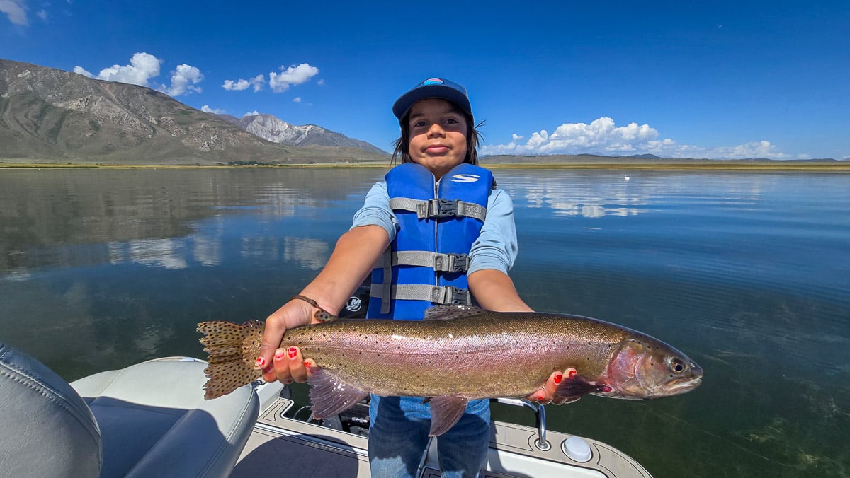 A fly fisherman holding a large rainbow trout on Crowley Lake near Mammoth Lakes, CA