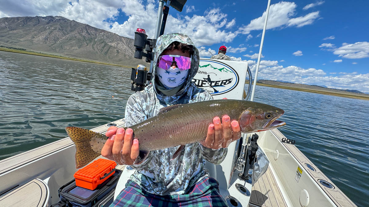 A fly fisherman holding a large brown trout on Crowley Lake near Mammoth Lakes, CA