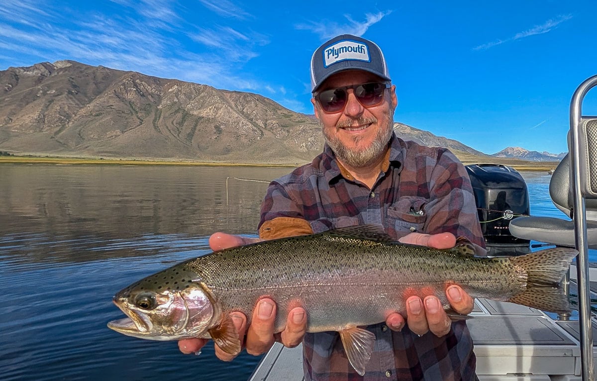 A fly fisherman holding a large rainbow trout on Crowley Lake near Mammoth Lakes, CA