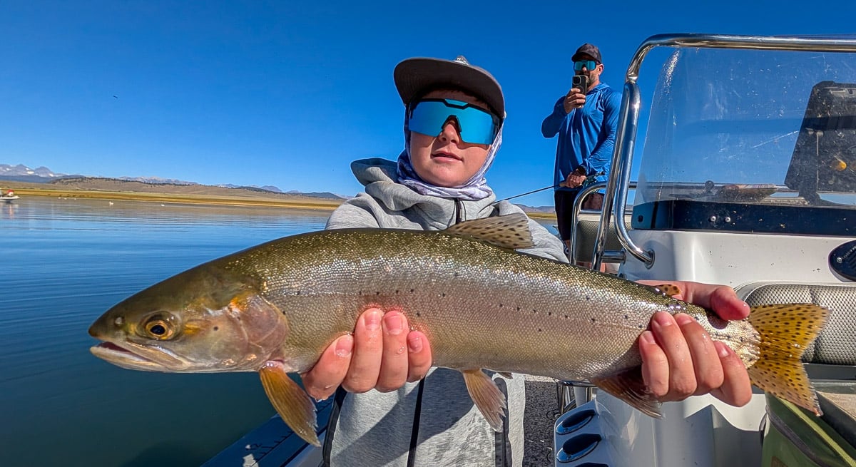 A fly fisherman holding a large rainbow trout on Crowley Lake near Mammoth Lakes, CA
