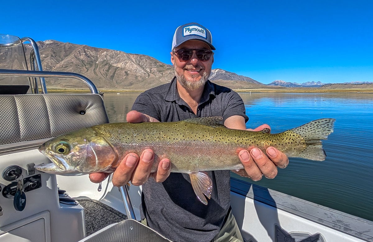 A fly fisherman holding a large rainbow trout on Crowley Lake near Mammoth Lakes, CA