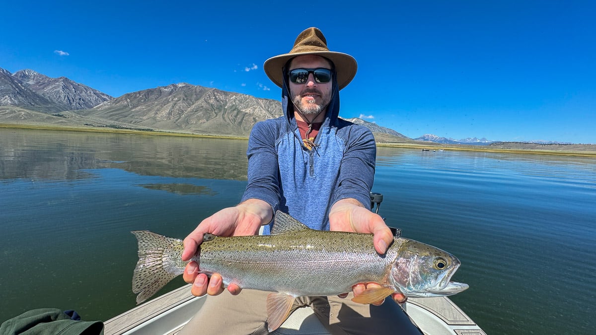 A fly fisherman holding a large rainbow trout on Crowley Lake near Mammoth Lakes, CA