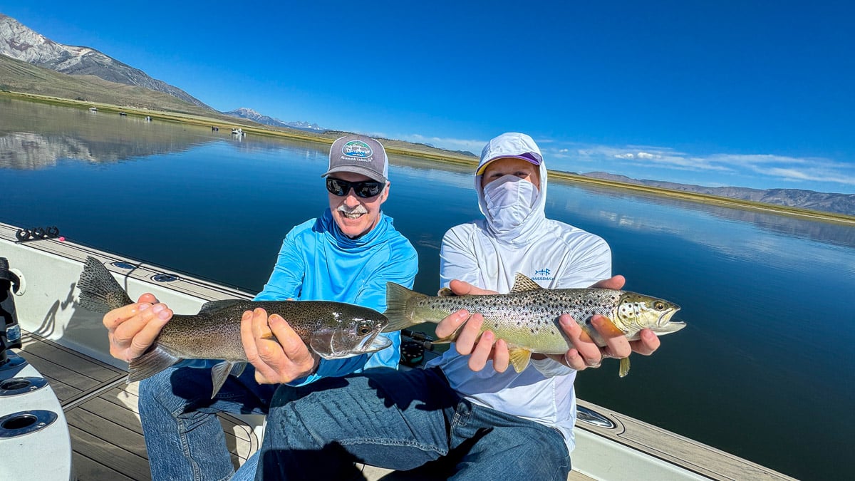 A smiling fly fisherman holding a large rainbow trout on the Crowley Lake near Mammoth Lakes, CA.