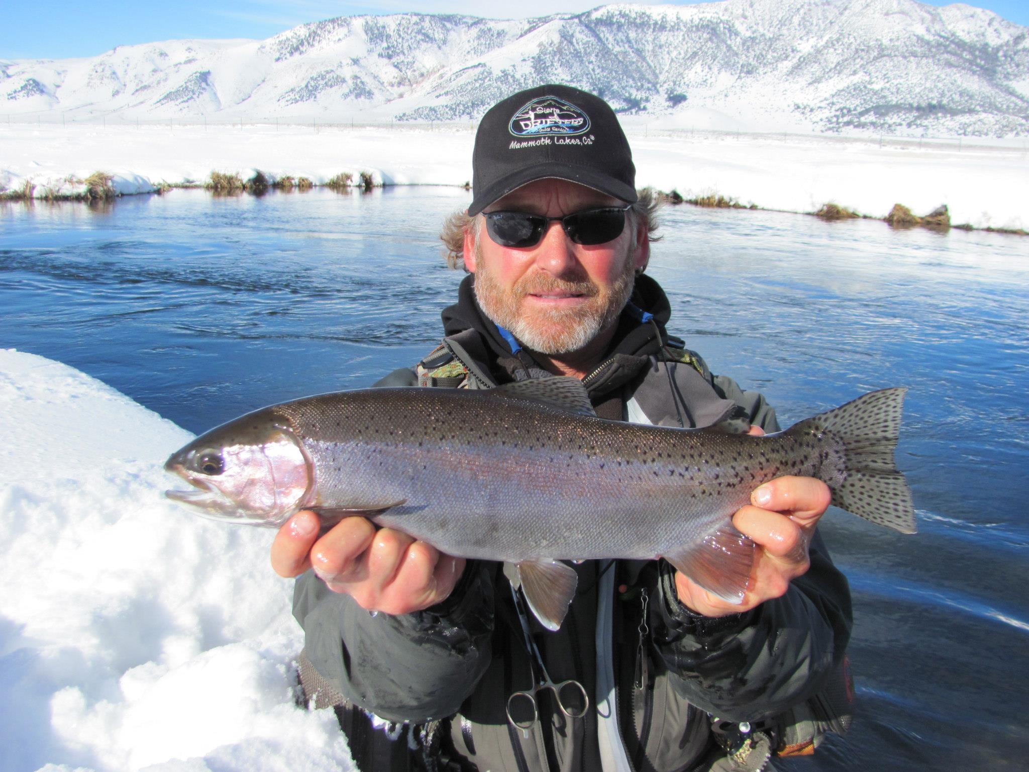 A smiling fly fisherman holding a large rainbow trout on the Crowley Lake near Mammoth Lakes, CA.