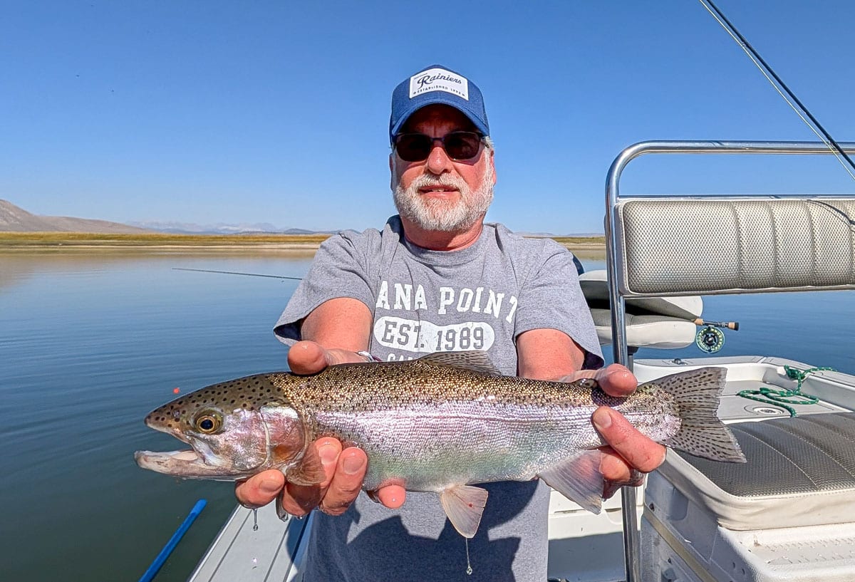 A smiling fly fisherman holding a large brown trout on the Crowley Lake near Mammoth Lakes, CA.
