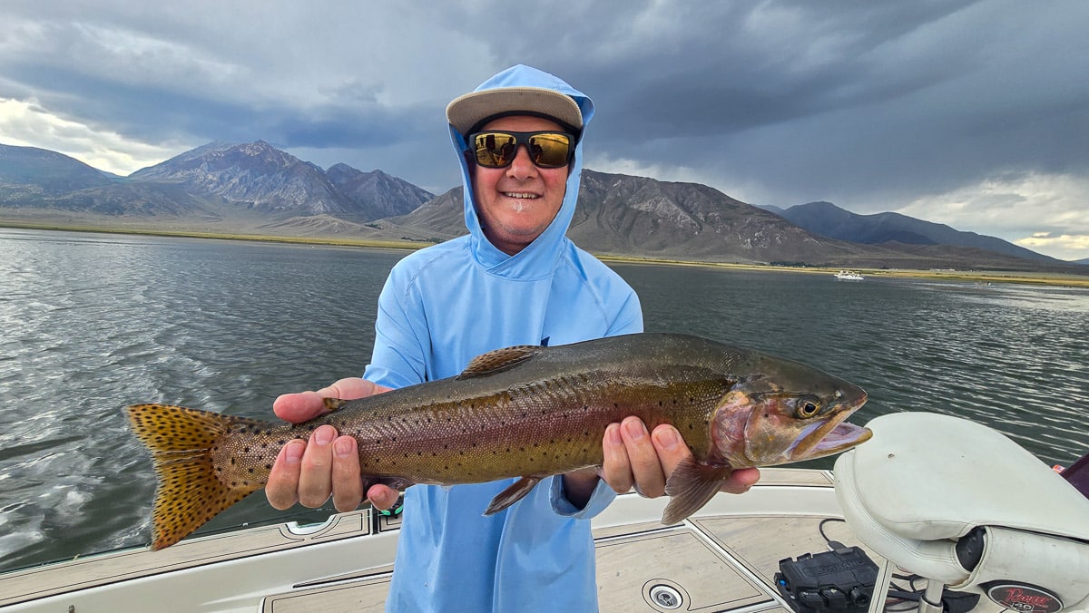 A fly fisherman holding a large brown trout on Crowley Lake near Mammoth Lakes, CA