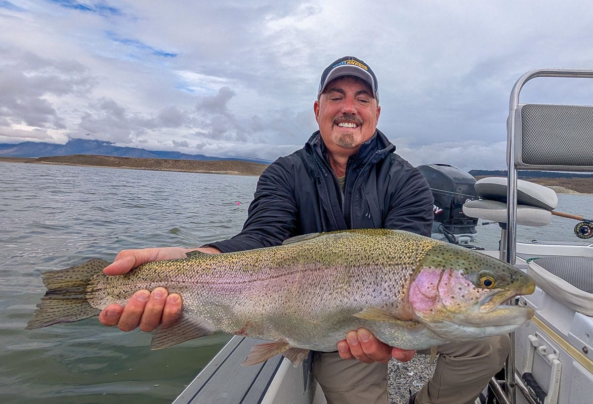 A fly fisherman holding a large rainbow trout on Crowley Lake near Mammoth Lakes, CA