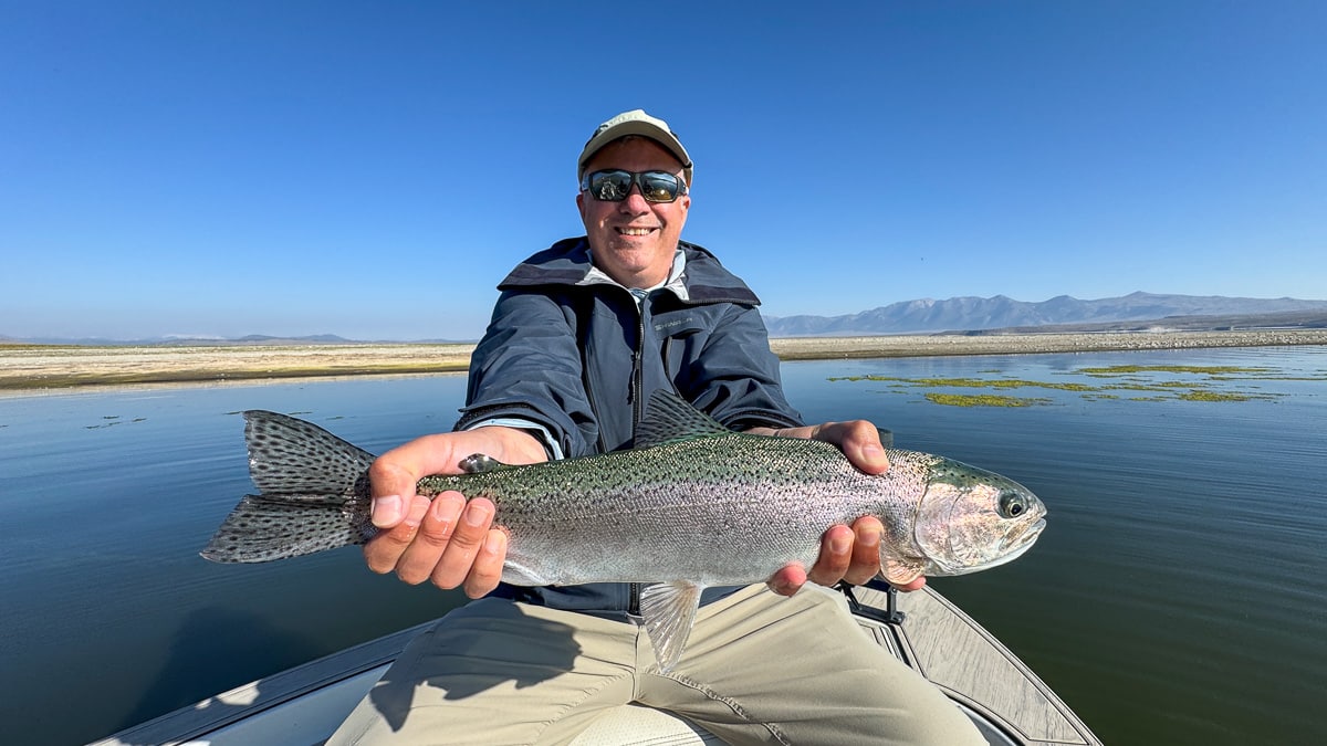 A smiling fly fisherman holding a large brown trout on the Crowley Lake near Mammoth Lakes, CA.