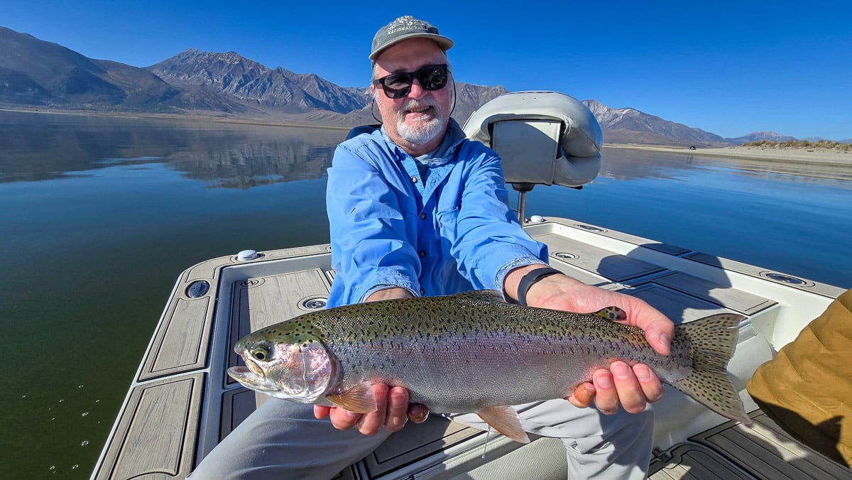 A fly fisherman holding a large rainbow trout on Crowley Lake near Mammoth Lakes, CA