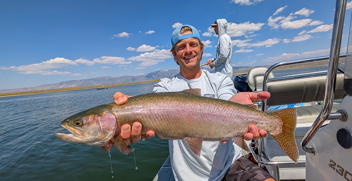 A smiling fly fisherman holding a large rainbow trout on the Crowley Lake near Mammoth Lakes, CA.