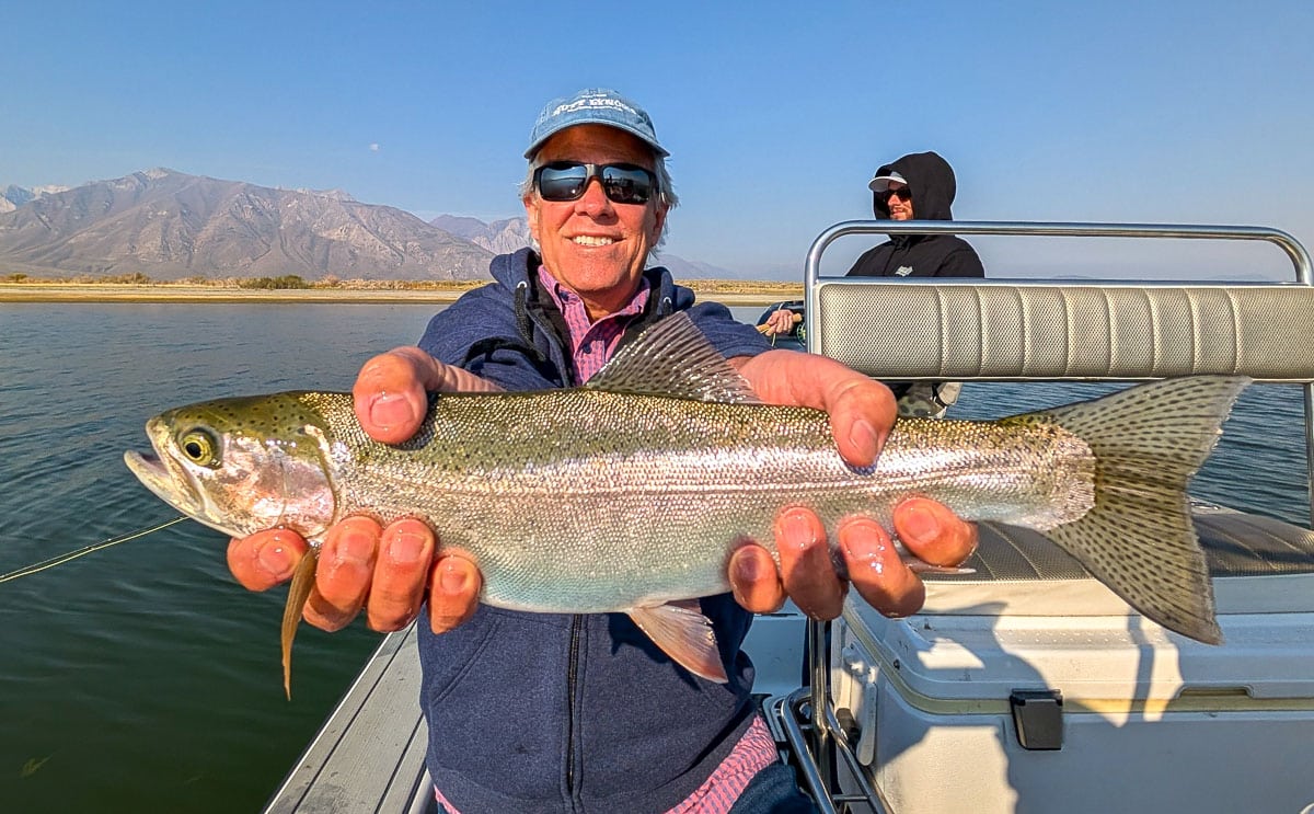 A smiling fly fisherman holding a large brown trout on the Crowley Lake near Mammoth Lakes, CA.