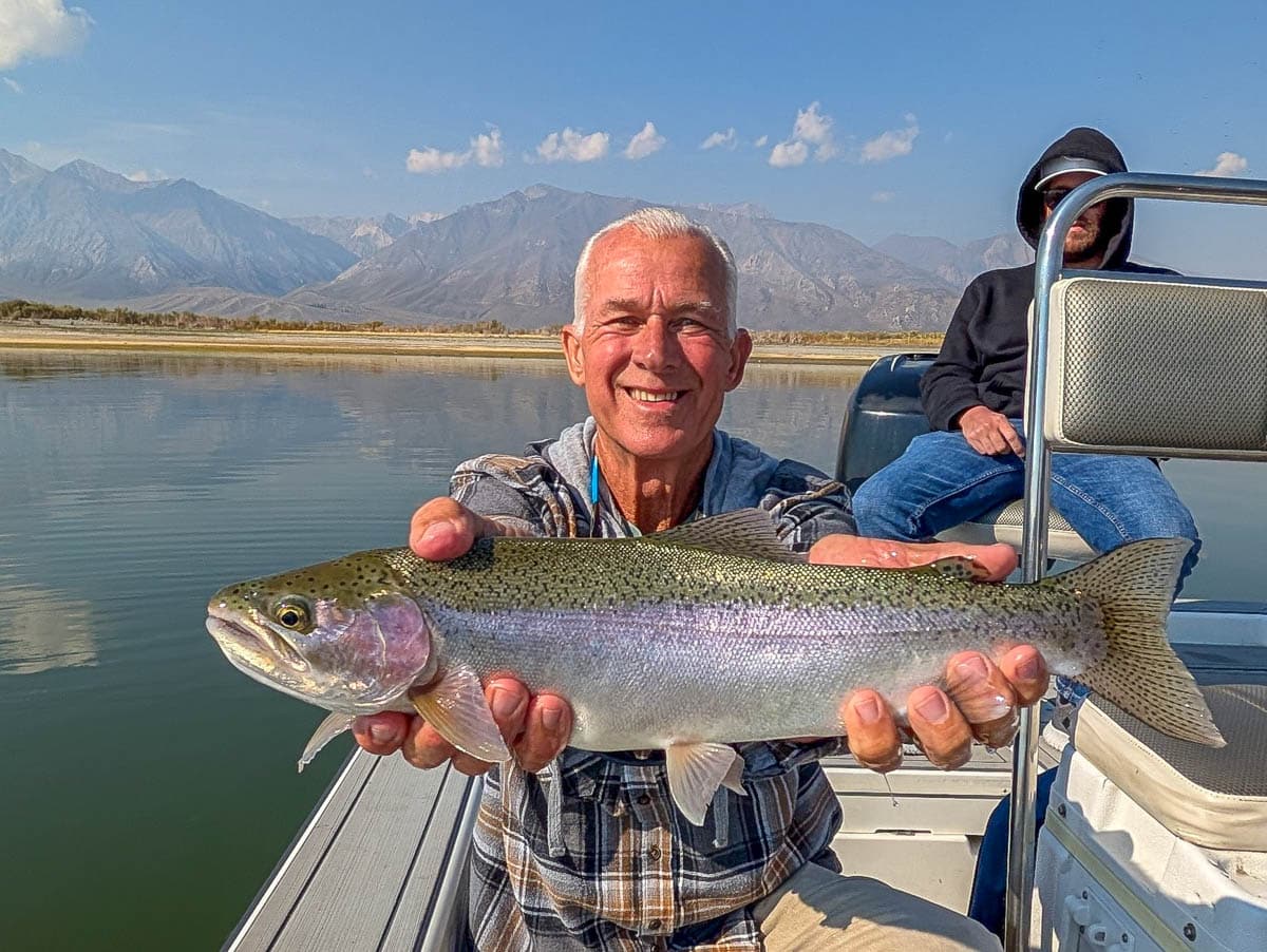 A fly fisherman holding a large rainbow trout on Crowley Lake near Mammoth Lakes, CA