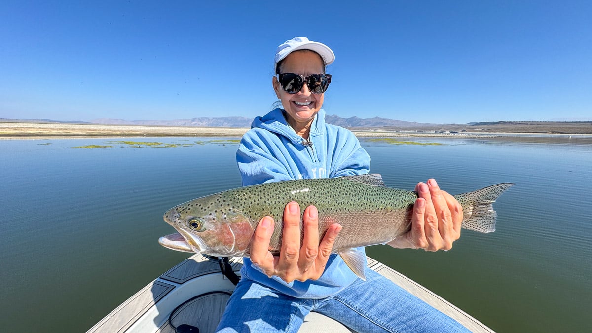 A fly fisherman holding a large rainbow trout on Crowley Lake near Mammoth Lakes, CA