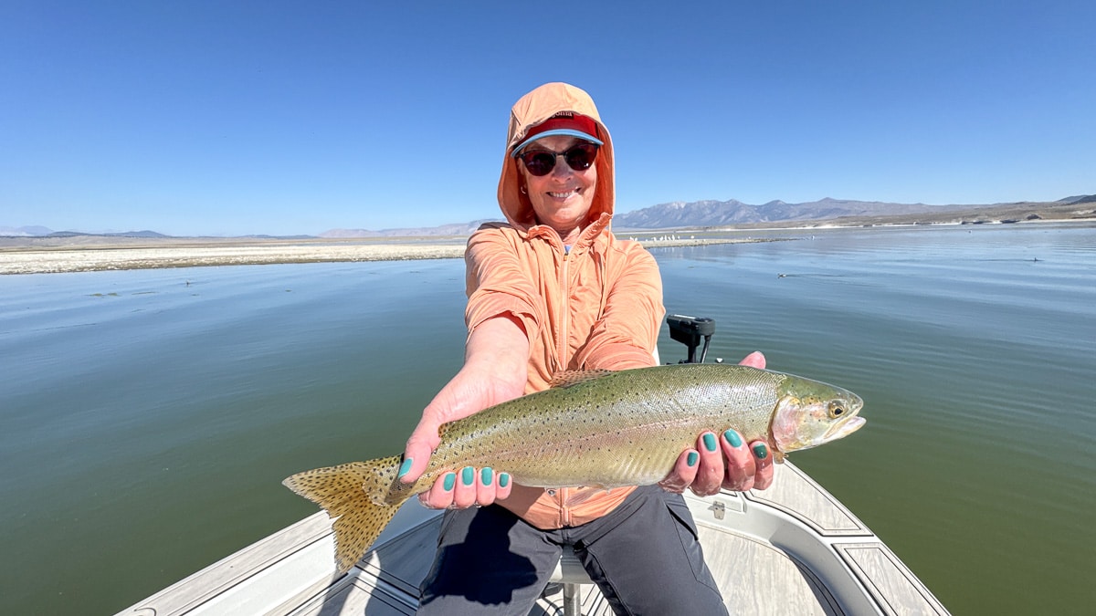 A fly fisherwoman holding a large rainbow trout on Crowley Lake near Mammoth Lakes, CA