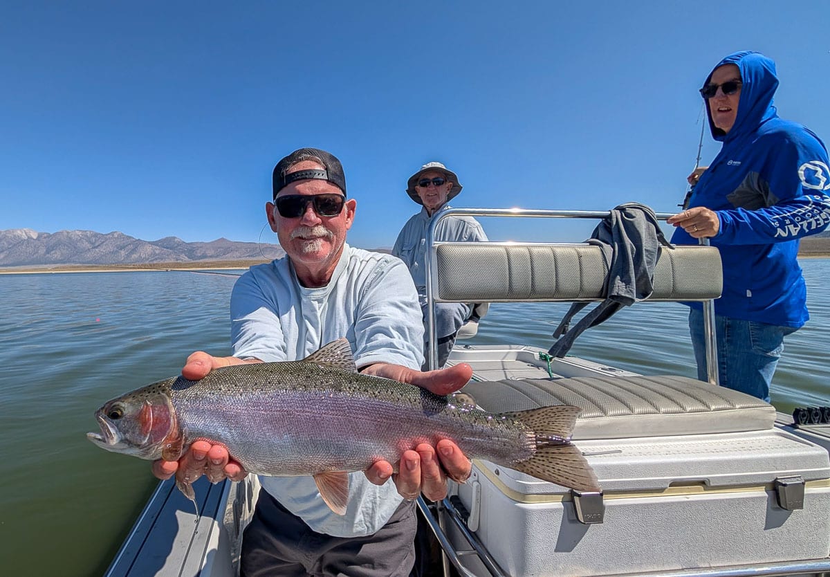 A fly fisherman holding a large brown trout on Crowley Lake near Mammoth Lakes, CA