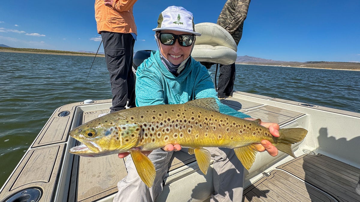 A smiling fly fisherman holding a large rainbow trout on the Crowley Lake near Mammoth Lakes, CA.