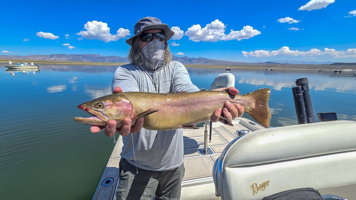 A smiling fly fisherman holding a large brown trout on the Crowley Lake near Mammoth Lakes, CA.