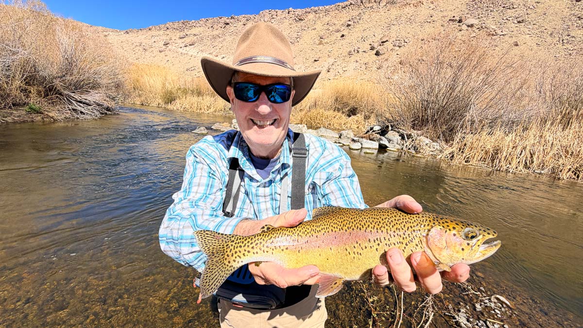 A fly fisherman holding a rainbow trout on the Lower Owens River near Bishop, CA