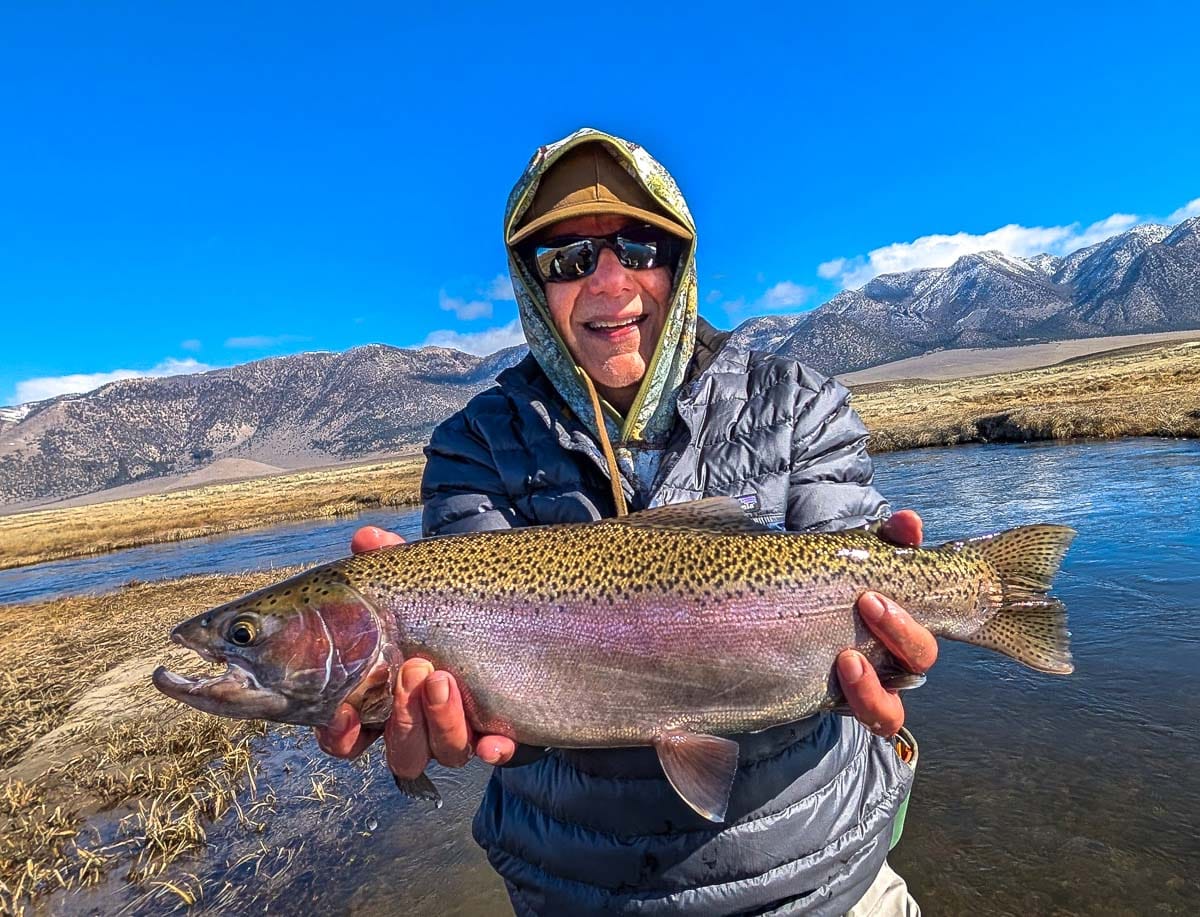 A fly fisherman holding a large rainbow trout on the Upper Owens River near Mammoth Lakes, CA