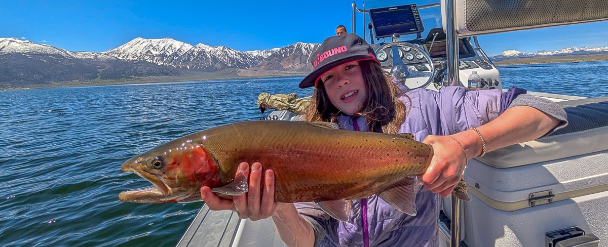 A fly fisherman holding a cutthroat trout in a boat on Crowley Lake near Mammoth Lakes, CA