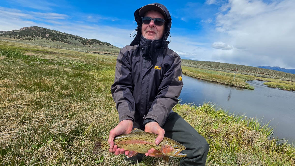 A fly fisherman holding a large rainbow trout on the Hot Creek River near Mammoth Lakes, CA