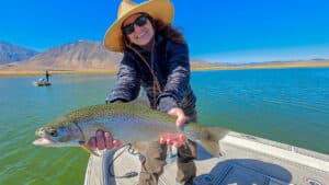 A fly fisherman holding a large rainbow trout in a boat on Crowley Lake near Mammoth Lakes, CA