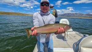 A fly fisherman holding a large cuthhroat trout in a boat on Crowley Lake near Mammoth Lakes, CA