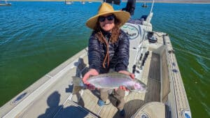 A fly fisherman holding a large rainbow trout in a boat on Crowley Lake near Mammoth Lakes, CA