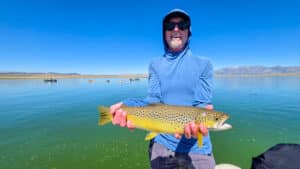 A fly fisherman holding a large brown trout in a boat on Crowley Lake near Mammoth Lakes, CA