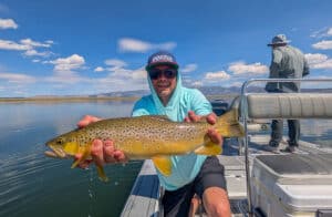 A fly fisherman holding a large brown trout in a boat on Crowley Lake near Mammoth Lakes, CA