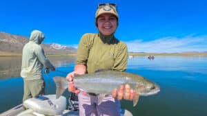 A fly fisherman holding a large rainbow trout in a boat on Crowley Lake near Mammoth Lakes, CA