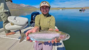 A fly fisherman holding a large rainbow trout in a boat on Crowley Lake near Mammoth Lakes, CA