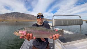 A fly fisherman holding a large rainbow trout in a boat on Crowley Lake near Mammoth Lakes, CA