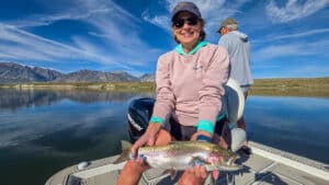 A fly fisherman holding a large rainbow trout in a boat on Crowley Lake near Mammoth Lakes, CA
