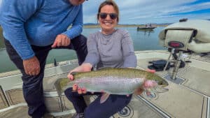A fly fisherman holding a large rainbow trout in a boat on Crowley Lake near Mammoth Lakes, CA