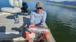 A fly fisherman holding a large rainbow trout in a boat on Crowley Lake near Mammoth Lakes, CA